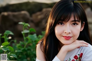 A woman with long black hair and pink nails leaning against a wooden wall.