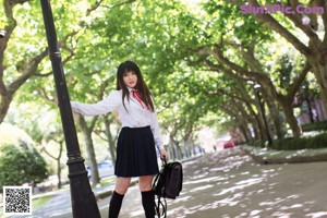 A woman in a school uniform leaning against a tree.