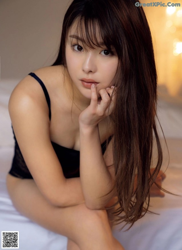 A woman in a black lingerie sitting on a bed.