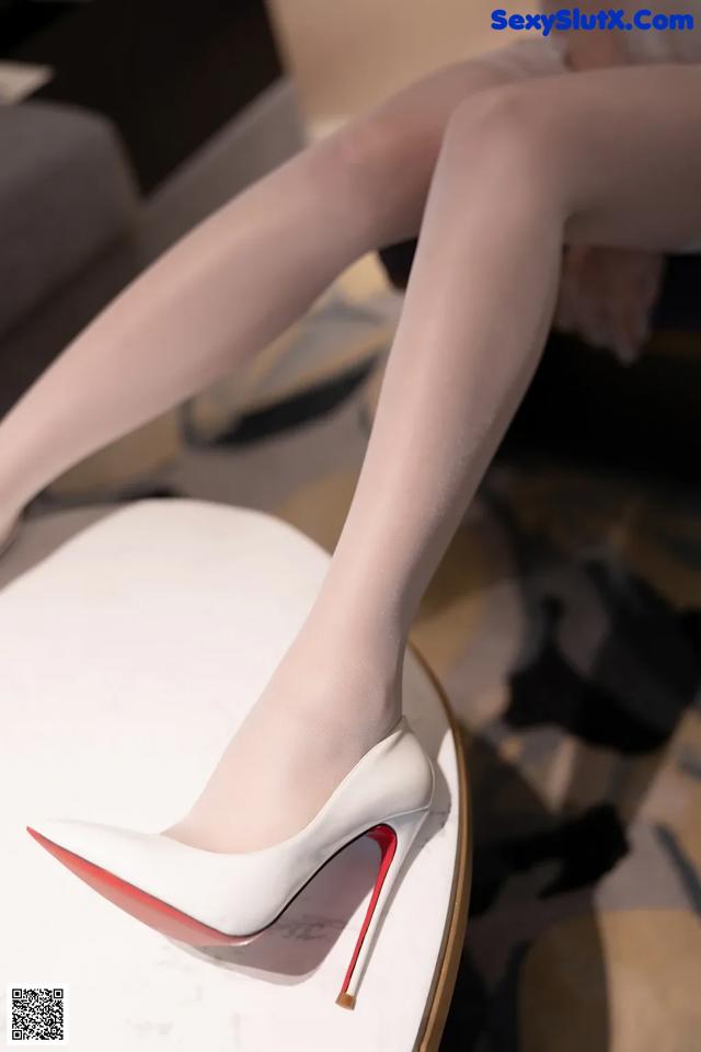 A woman wearing white stockings and high heels sitting on a table.