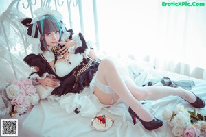 A woman in a maid outfit sitting on a bed.