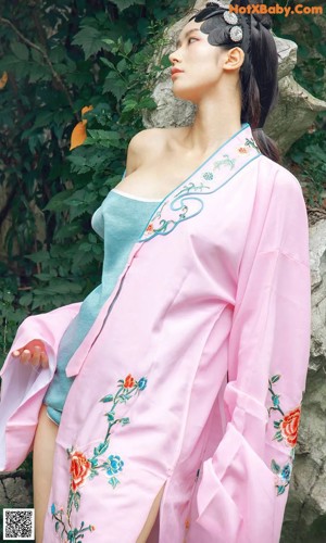 A woman in a white dress sitting on a wooden floor next to a flower.