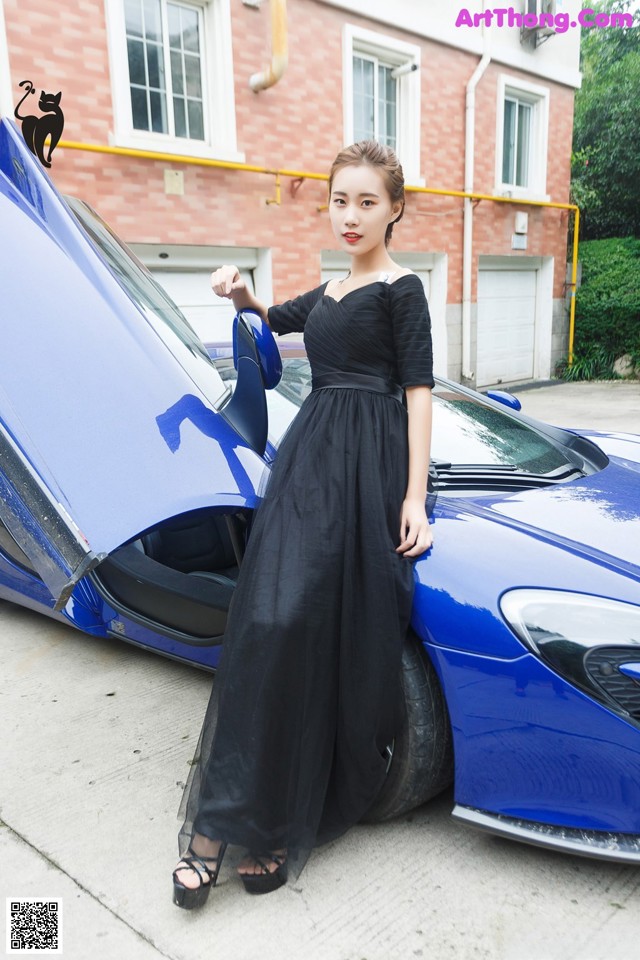 A woman in a black dress standing next to a blue car.