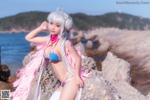 A woman in a bikini sitting on a rock by the ocean.