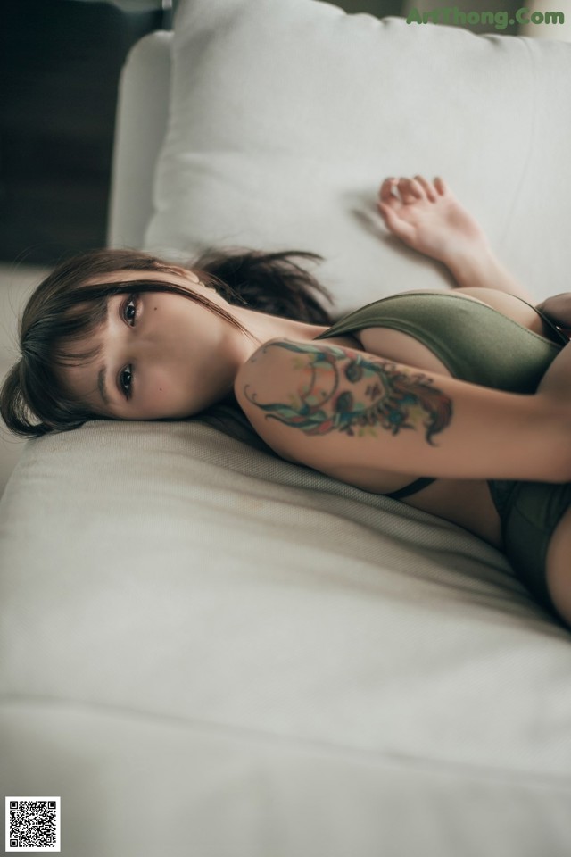 A woman laying on a white couch with a tattoo on her arm.