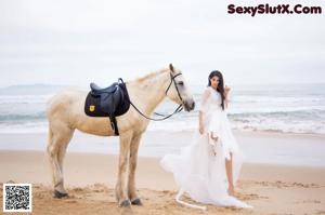 A woman in a yellow bikini standing next to a white horse.