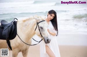 A woman in a white dress riding a white horse on the beach.