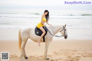 A woman in a yellow dress standing next to a white horse.