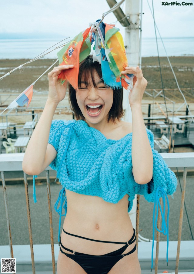 A woman in a blue top and black bikini holding a colorful hat.