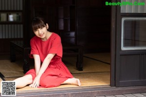 A woman sitting on a bed in front of a window.