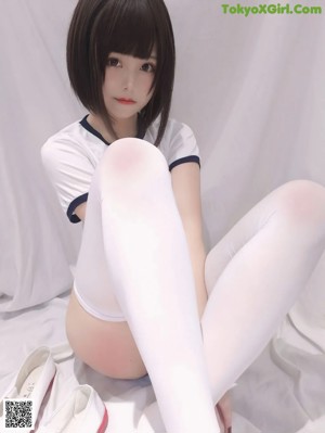 A woman in white stockings and high heels is sitting on a bed.
