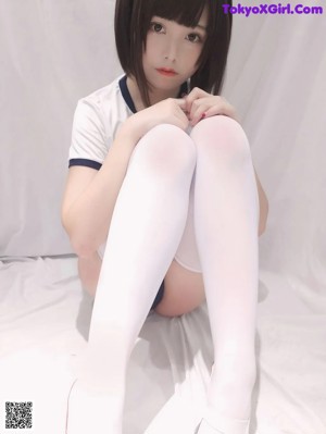 A woman in a white shirt and black panties sitting on a bed.