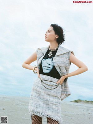 A woman standing next to a white horse on a beach.