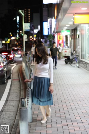 A woman in a blue shirt is standing by a window.