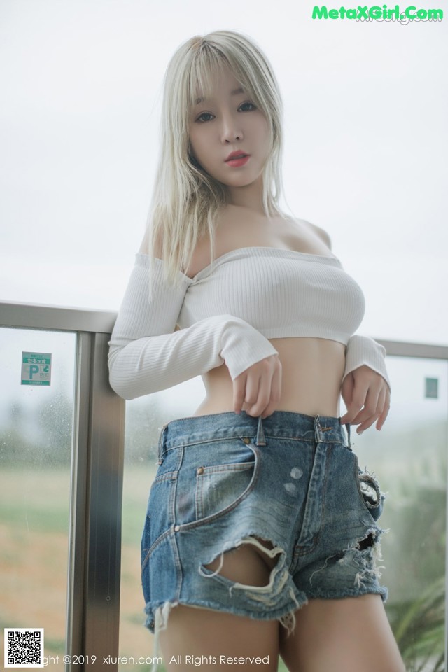 A woman in a white top and denim shorts posing for a picture.