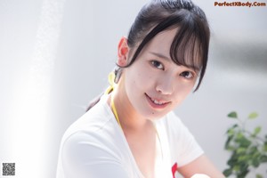 A woman in a white shirt and yellow bikini sitting on the floor.