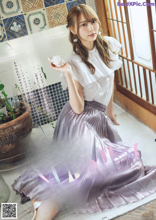 A woman in a white shirt and purple skirt sitting on the floor.