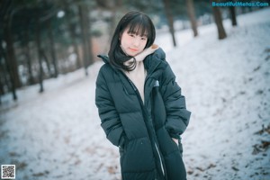 A woman leaning against a tree in the snow.