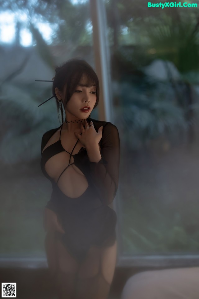 A woman in a black dress standing in front of a window.