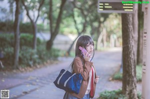 A woman in a school uniform holding a cell phone.