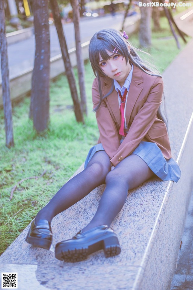 A woman in a school uniform sitting on a ledge.