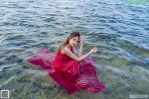 A woman in a red dress standing in the water.