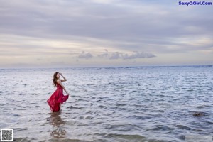 A woman in a red dress standing on a beach.