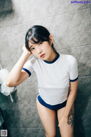 A woman in a white shirt and blue shorts standing in a bathroom.