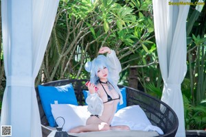 A woman in a white dress sitting on a towel by a pool.