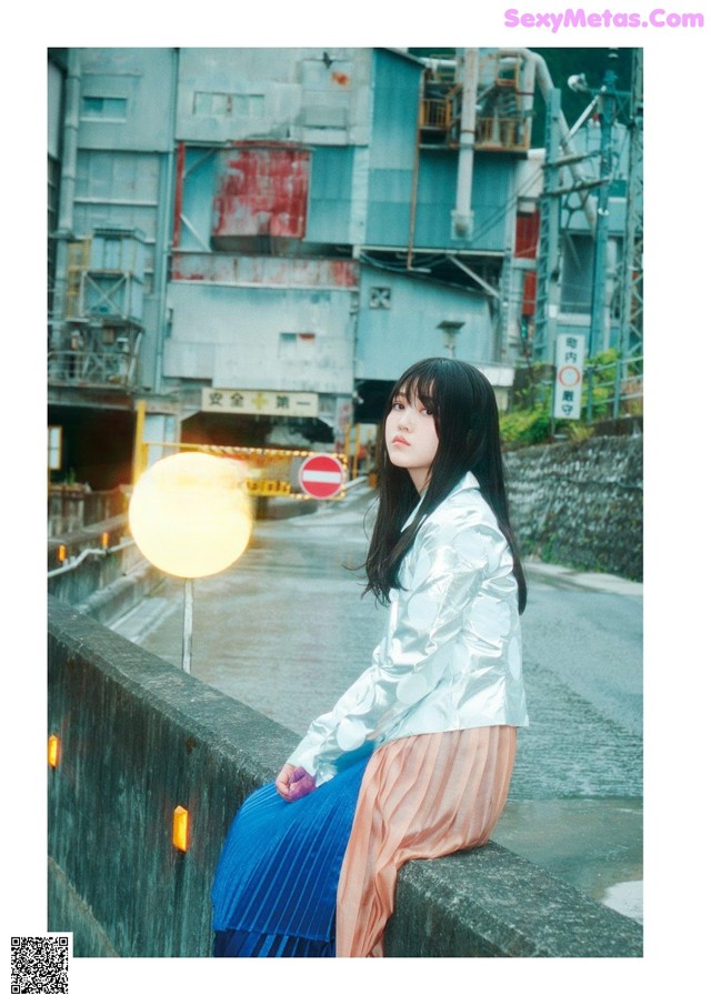 A woman sitting on a wall next to a street sign.