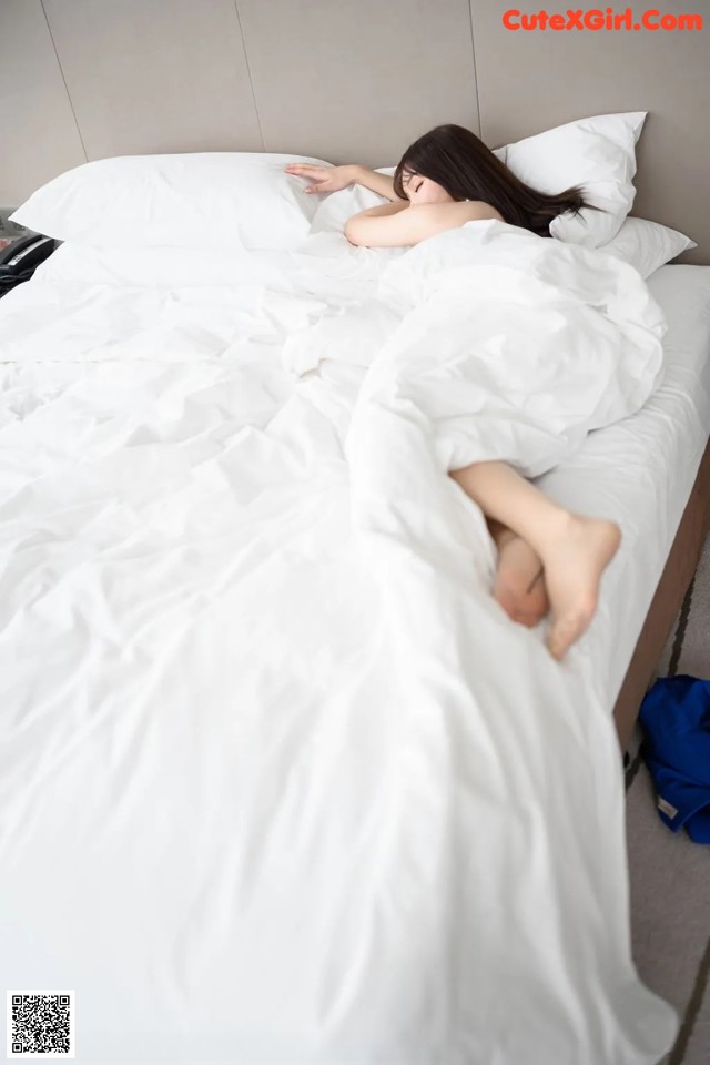 A woman laying on a bed covered in white sheets.