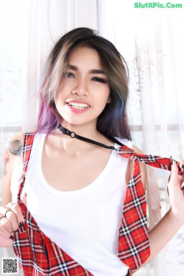 A woman with purple hair wearing a white tank top and red plaid skirt.