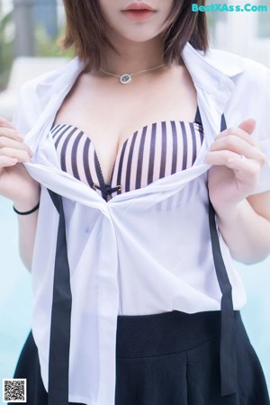 A woman in a white shirt and black skirt posing by a pool.