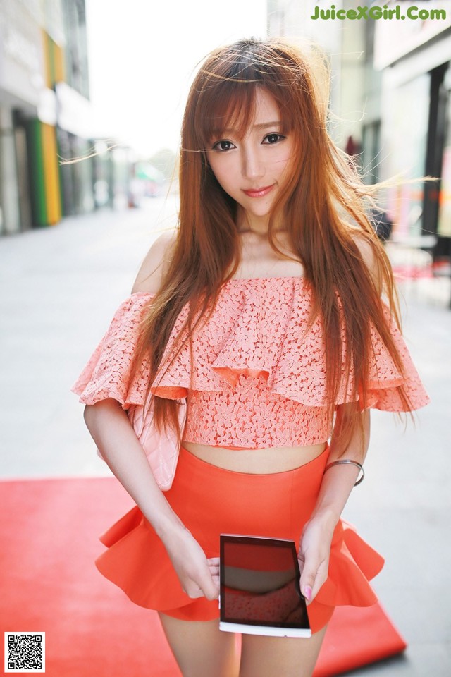 A woman in a pink top and orange skirt holding a tablet.