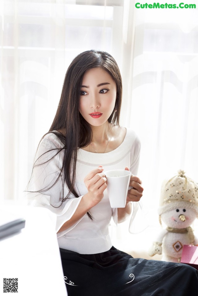 A woman sitting on a couch holding a cup of coffee.