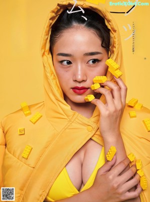 A woman in a yellow lingerie sitting on a yellow wall.