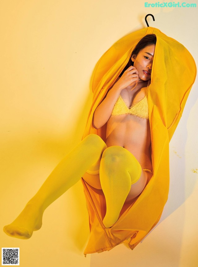 A woman in a yellow lingerie sitting on a yellow wall.