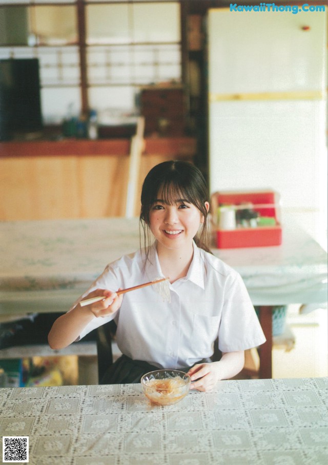 A woman sitting at a table with chopsticks in her hand.