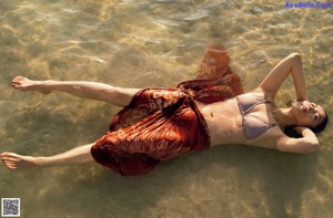 A woman in a black bikini standing in the water.