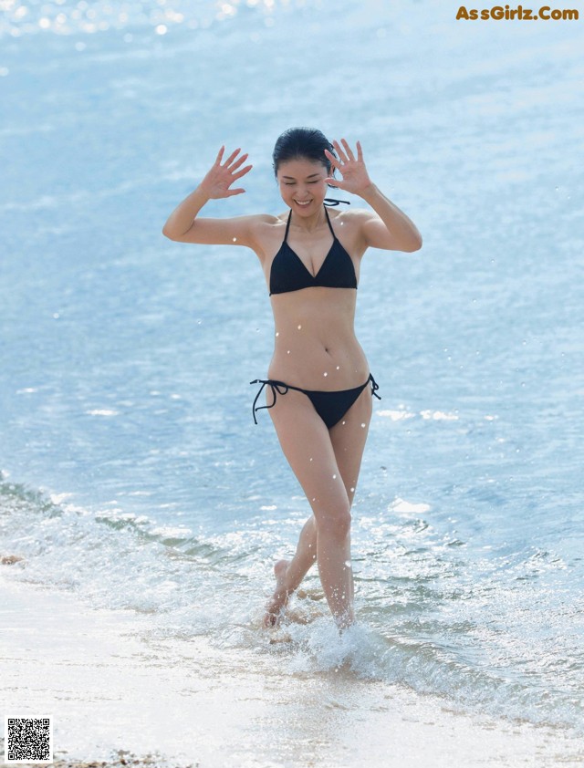 A woman in a black bikini running into the ocean.