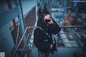 A woman in a black jacket and cat ears sitting on a metal structure.