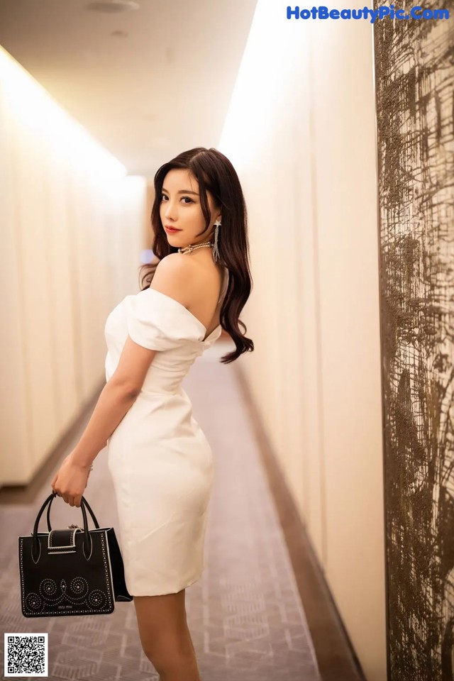 A woman in a white dress holding a black handbag.