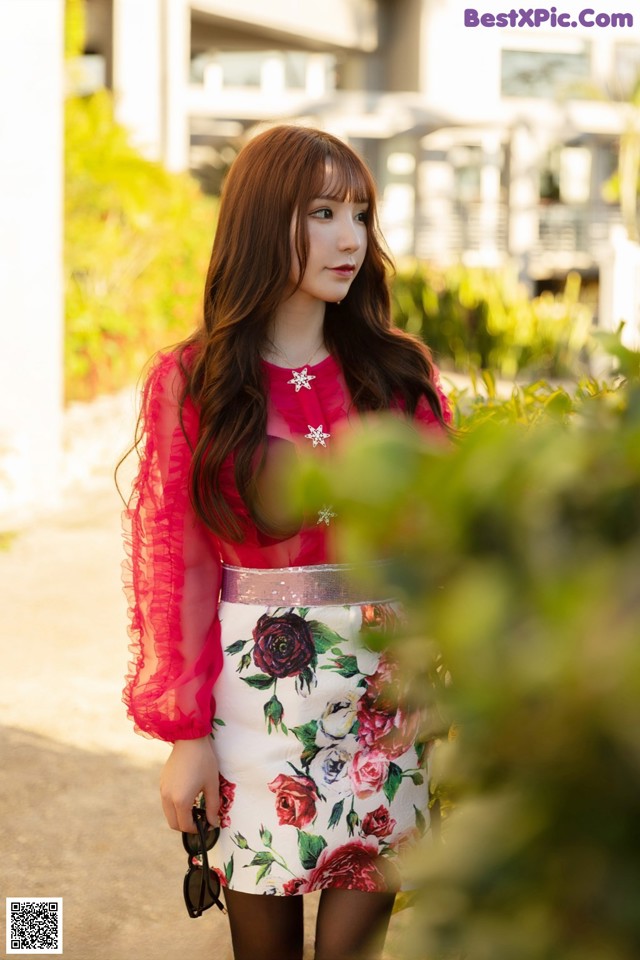 A woman in a pink top and floral skirt posing for a picture.