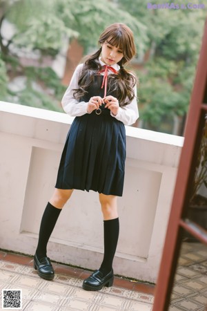 A woman in a school uniform leaning against a wall.