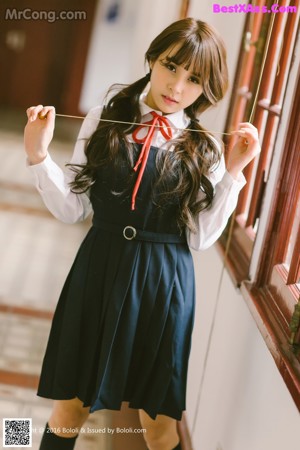 A woman in a school uniform leaning against a fence.