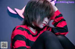 A woman in a red and black striped dress sitting on a bed.