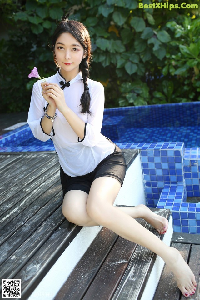 A woman sitting on a wooden bench next to a swimming pool.