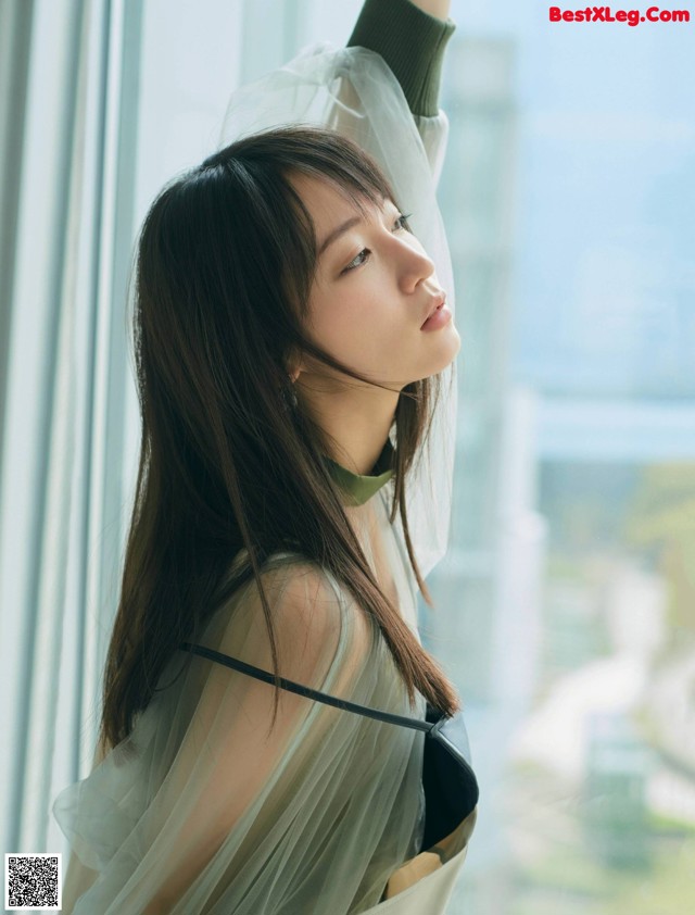 A woman standing by a window with her hand on the window sill.