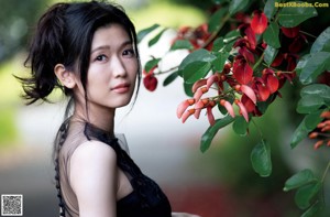 A woman holding a red flower in front of her face.