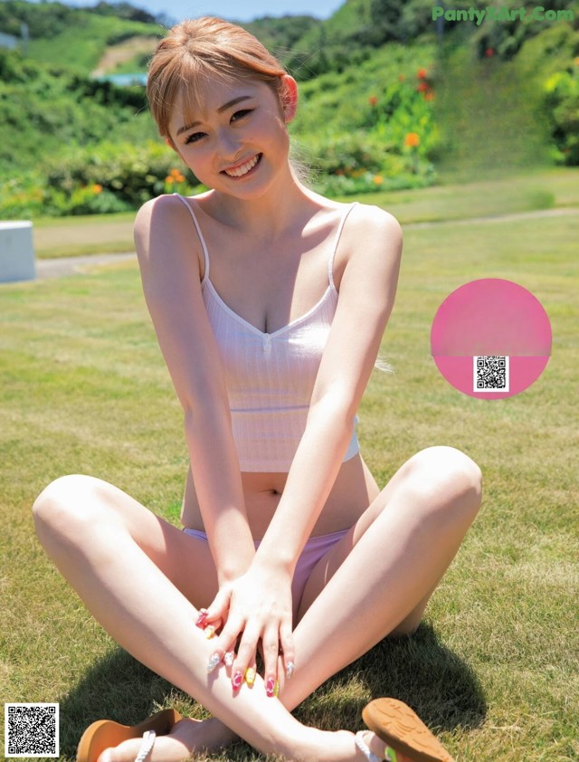 A woman in a white bikini sitting on the grass.